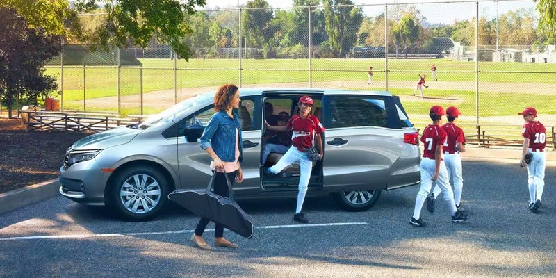 An all new Gray 2024 Honda Odyssey parked at a baseball field parking lot while kids get out of the van. - Boyd Honda Oxford, NC