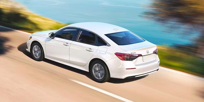 An all-new White 2024 Honda Civic Sedan cruising an oceanside highway. - Boyd Honda Oxford, NC