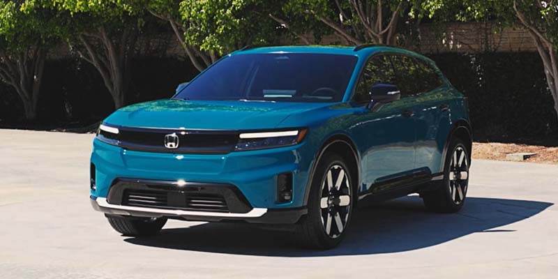An all new Blue 2024 Honda Prologue parked in front of some trees and a retaining wall. - Boyd Honda Oxford, NC