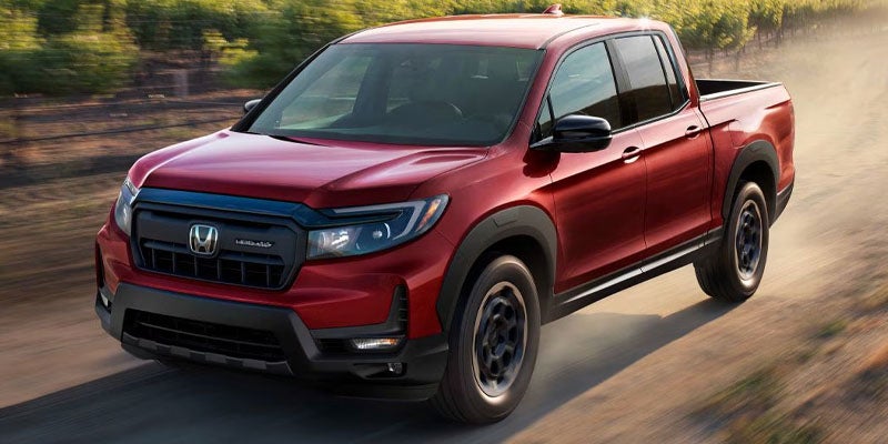 An all-new Red 2024 Honda Ridgeline cruising along a dirt road. - Boyd Honda Oxford, NC