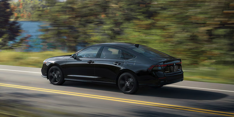 An all-new black Honda Accord Hybrid cruising along a waterside highway. - Boyd Honda Oxford, NC