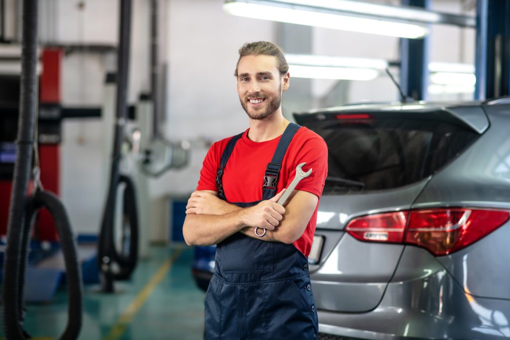 A mechanic smiling and holding a wrench in a garage.