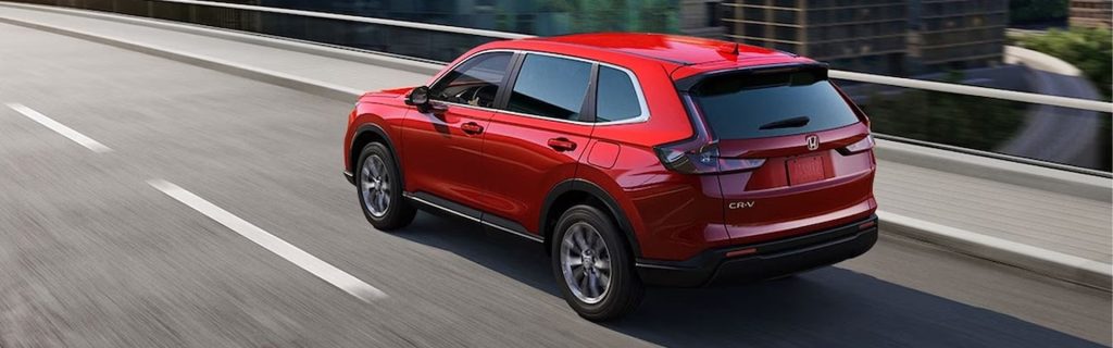 Red Honda CR-V driving on a city highway, showcasing its modern design and everyday versatility.