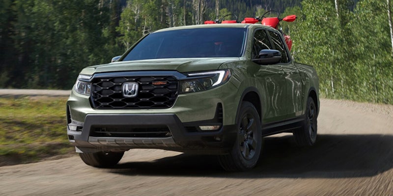 Green Honda Ridgeline pickup truck driving on a dirt road surrounded by trees.