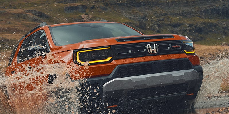 An orange Honda Accord splashing through muddy water on a rugged mountain trail.