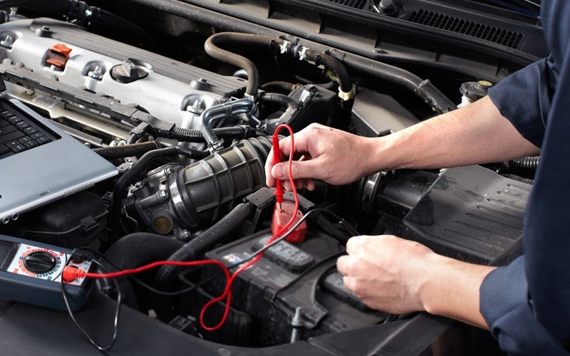 A mechanic tests a car battery with a multimeter under the hood.