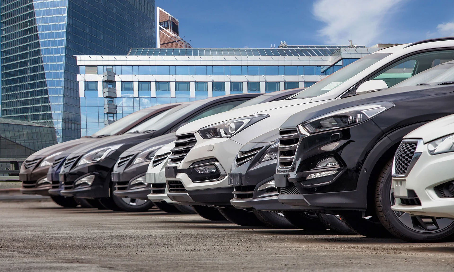 A row of parked cars outside a modern glass office building.